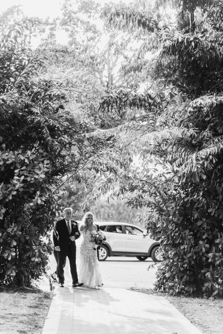A black and white photo of two people walking through the trees.