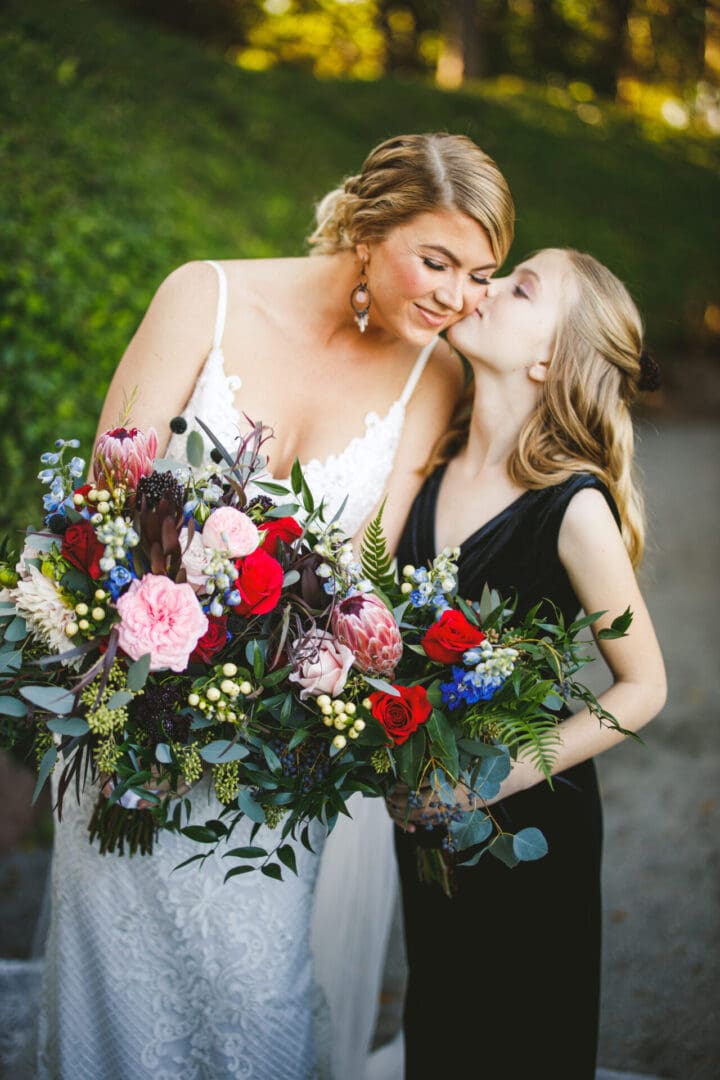 Two women kissing each other while holding a bouquet of flowers.