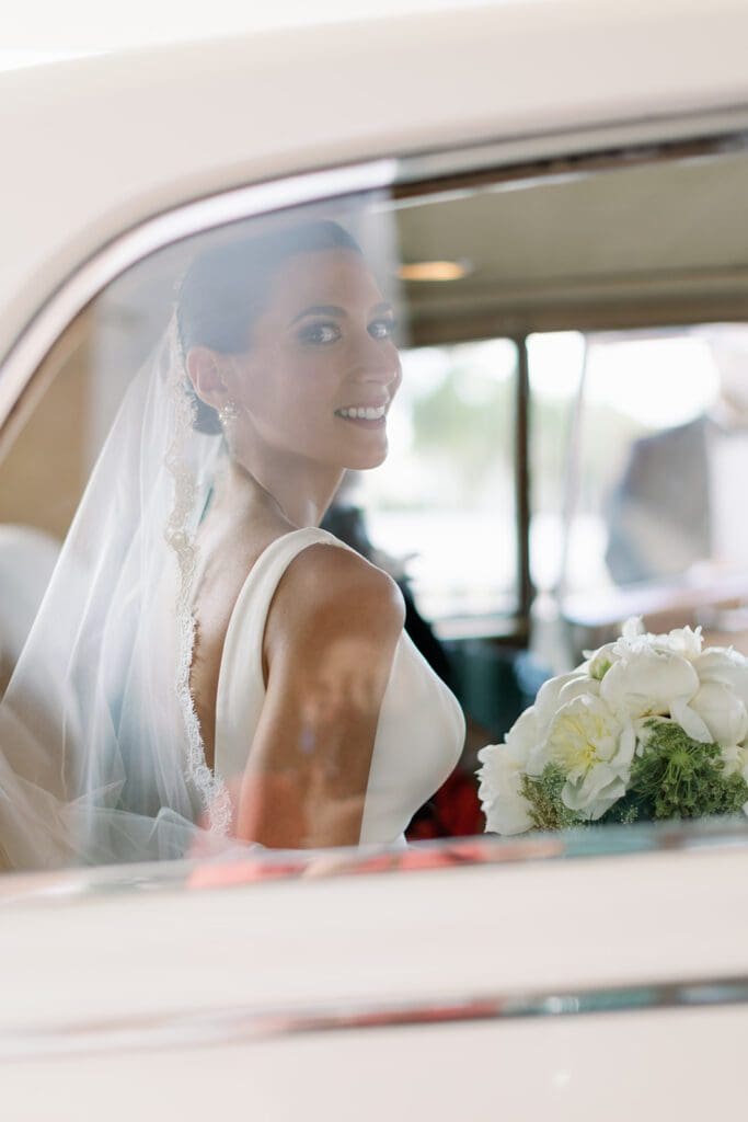 A bride sitting in the back of her car.