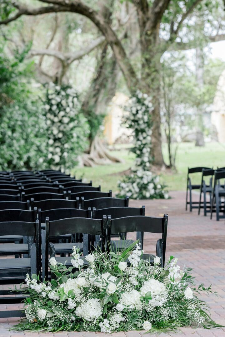 A row of black chairs with white flowers in them.