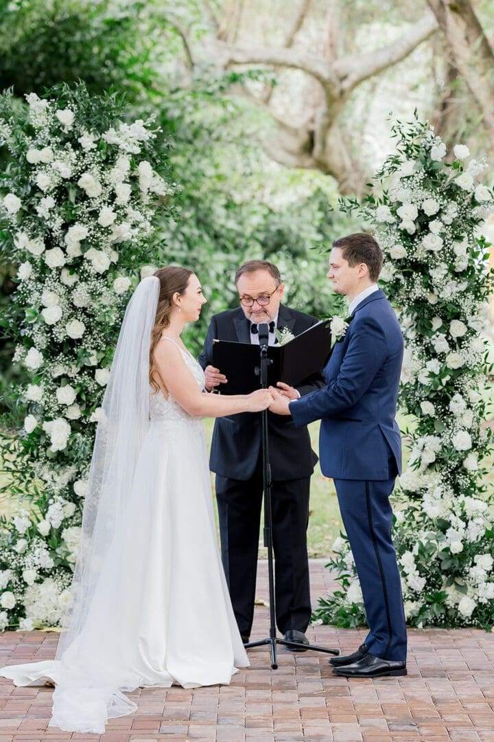 A couple getting married under an arch of flowers.