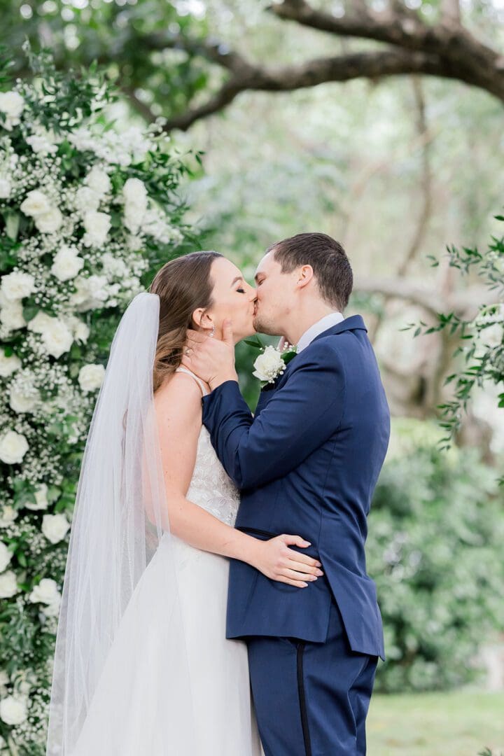 A bride and groom kissing in front of white flowers.
