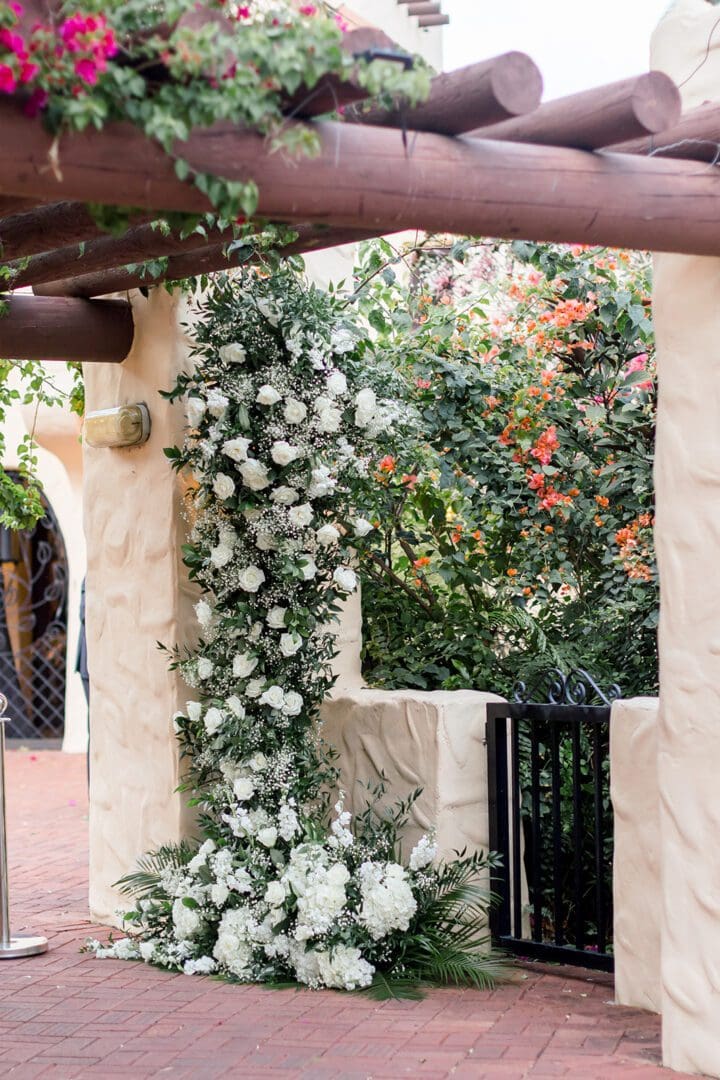 A white flower covered arch in front of trees.