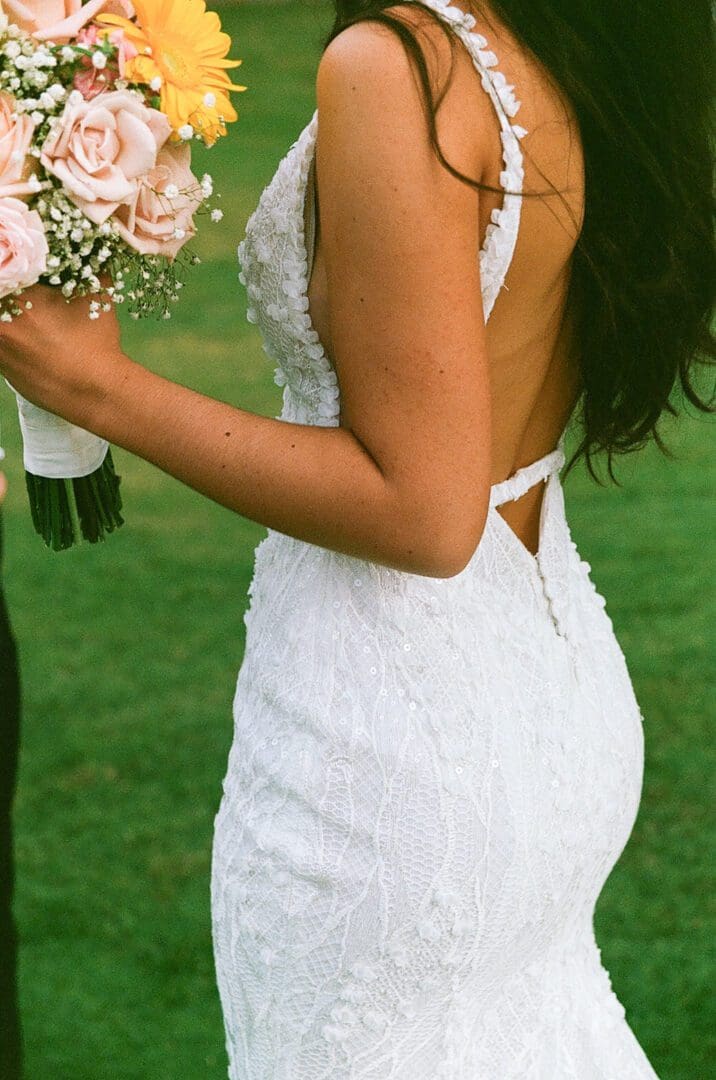 A woman in white dress holding flowers and wearing a black suit.