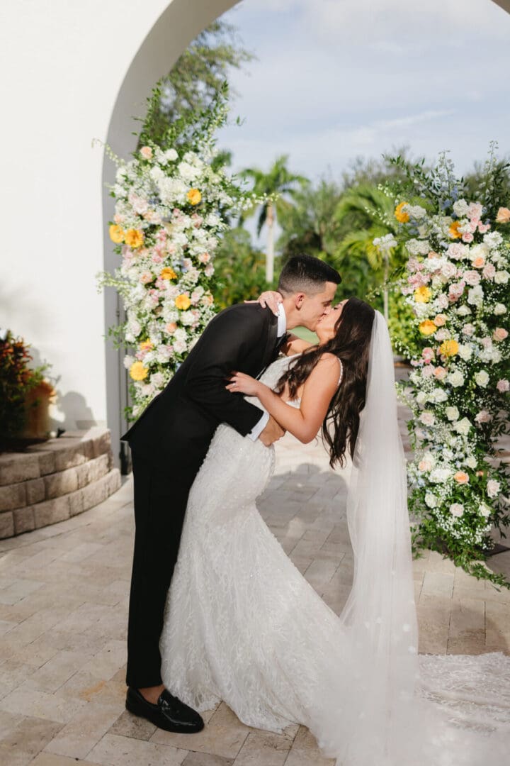 A couple kissing in front of a floral arch.