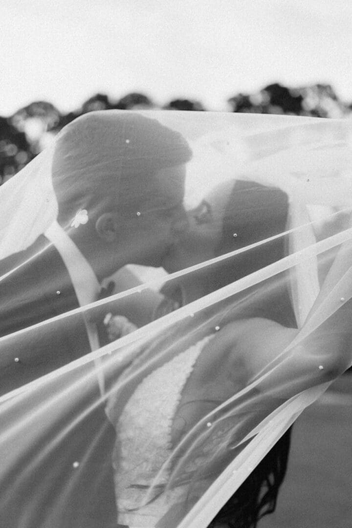 A man and woman kissing under the veil of their wedding car.