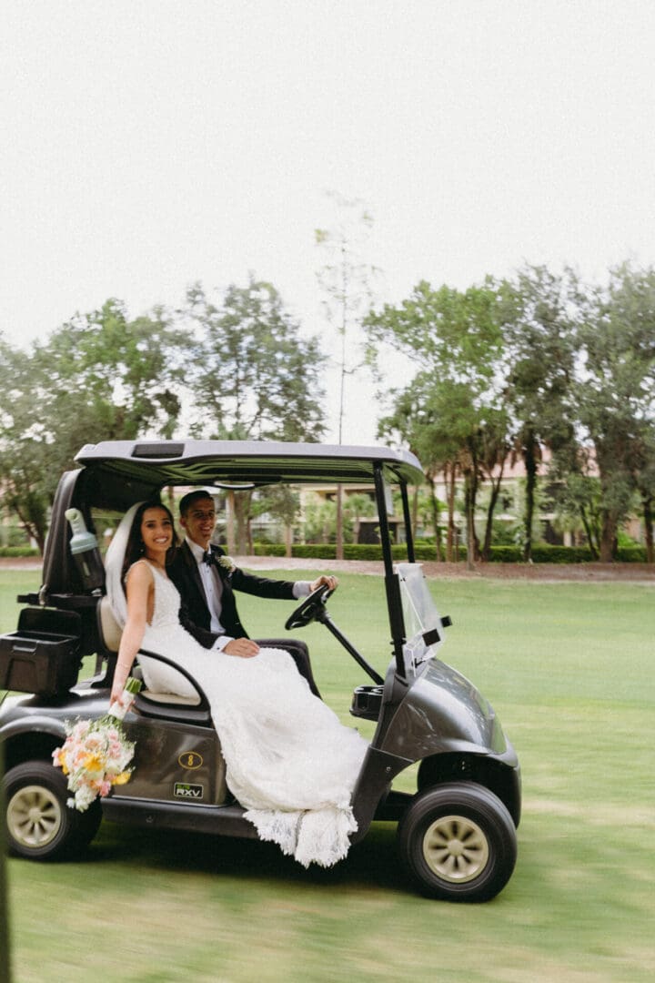 A bride and groom in the back of a golf cart.
