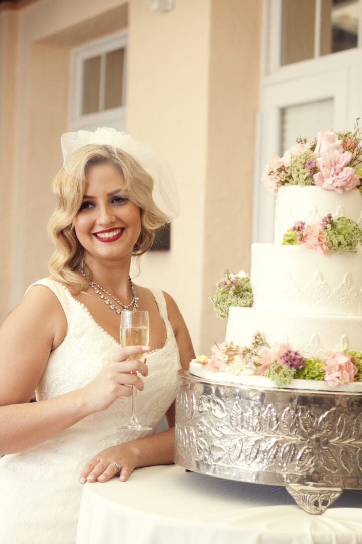 A woman holding a glass in front of a cake.