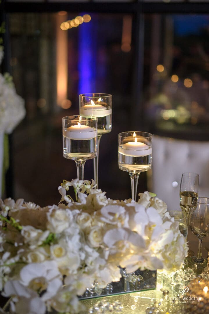 A table with white flowers and candles in wine glasses.