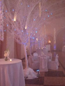 A room with tables and chairs, white trees and lights.